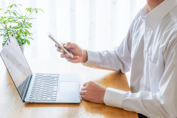 オンライン業務中の男性がスマートフォンを操作するビジネスシーン