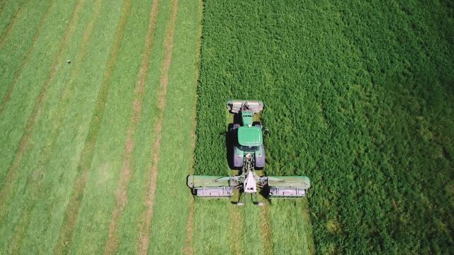 High-tech tractor works in agriculture, technical equipment of farm. Mowing grass in agricultural field. Tractor with autopilot works with high-tech productive, technologically mower. Aerial view.
