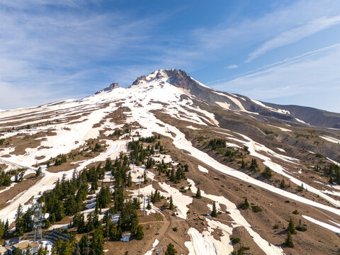 Aerial view of a snow-dusted mountain peak kissed by a clear blue sky, with patches of green forest clinging to its slopes, Government Camp, Oregon, United States.