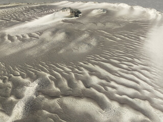 Aerial view of wind-sculpted sands create hypnotic patterns across the arid landscape, a solitary rock formation stands defiant against the elements, Namib Desert, Kunene Region, Namibia.