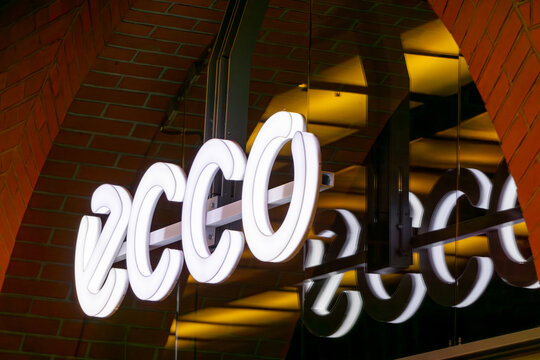 Illuminated ECCO shoe store sign above the entrance in a shopping center with brick facade
