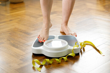 Female standing on bathroom scale with measurement tape on wooden floor