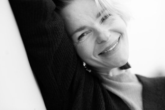 Black and white close-up of a smiling woman leaning into the frame with a soft, joyful expression