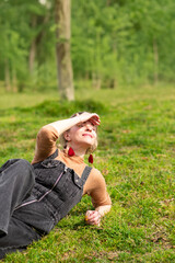 Obraz premium smiling woman lounges in a grassy forest clearing, shading her eyes from the sun with one hand