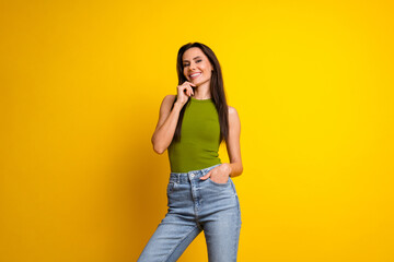 Charming woman in a green top and jeans posing against a vibrant yellow background, expressing confidence and happiness
