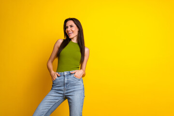 Smiling young woman with casual style standing confidently on a vibrant yellow background radiating...