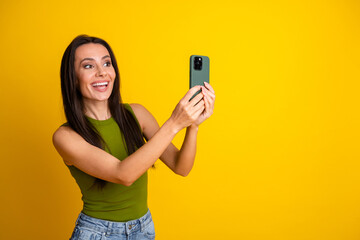 Smiling young woman holding smartphone on vibrant yellow background showcasing happiness and casual...