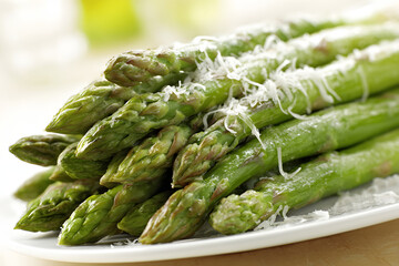 Pile of fresh green asparagus with grated parmesan cheese on a white plate.