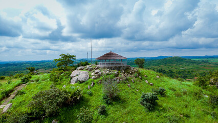 Aerial view of a hut on a hilltop surrounded by green grass and scattered rocks under a cloudy sky, Miango, Plateau, Nigeria.