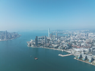 Fototapeta premium Jan 11, 2022 - Hong Kong, China: Aerial view of Hong Kong cityscape with Victoria Harbor, waterfront, urban buildings, and ocean under clear sky.