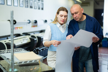 Woman and man looking at large format paper while working in printing office.