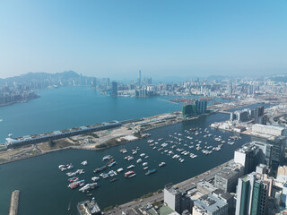 Obraz premium Breathtaking aerial view of central Hong Kong, China, displaying the vast cityscape, harbor with boats, and distant mountains under a clear sky.