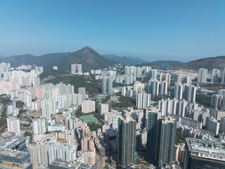 Fototapeta premium Aerial view of central Hong Kong, China, shows a dense cityscape with numerous buildings under a clear blue sky, mountains visible in the distance.
