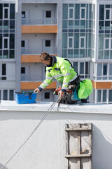 Construction Worker Painting a Building Roof: Attention to Safety and Precision in Urban Renovation
