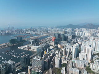 Fototapeta premium Aerial view of central Hong Kong, China, showcasing a dense cityscape. Buildings sprawl towards the harbor under a clear blue sky, with distant mountains.