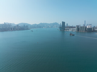 Obraz premium Aerial view of central Hong Kong, China, showcasing the vast harbor and cityscape. Buildings line the waterfront and distant mountains are visible under a clear sky.