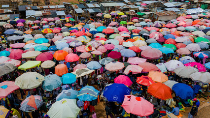 Jos, Nigeria - 28 July 2025: Aerial view of a bustling market, a vibrant tapestry of colorful umbrellas shading the dense crowd below, creating a mesmerizing spectacle of commerce and community..
