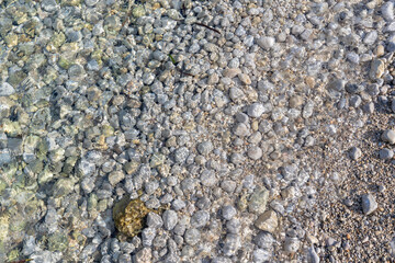 A delicate, transparent wave washes over the small gray rocks in the morning. Cala Xinxell is a beautiful beach with crystal-clear waters located in Illetes, Palma de Mallorca, Spain.