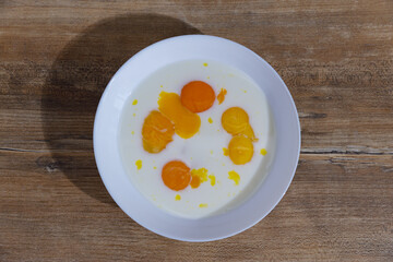 A Delicious Display of Fresh Egg Yolks and Cream Blended Together in a White Bowl Arranged on a Rustic Wooden Table for a Culinary Presentation, Perfect for Breakfast or Baking.