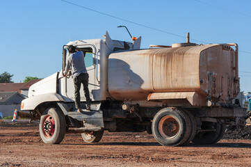 Worker climbing into a water truck at a construction site, used for dust control and soil...