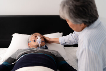 scene of bedridden patient, elderly hopeless senior man lying on bed with oxygen mask by doctor. home caregiver nurse visit retirement patient for health check up recovery process medical service