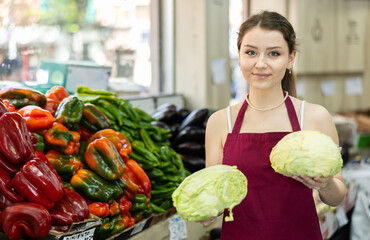 Grocery store female employee places ripe cabbage on a display case at a supermarket