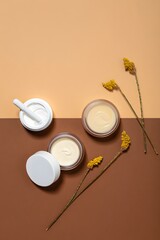 Top view of natural skincare products and yellow flowers on brown and beige background flat lay shot