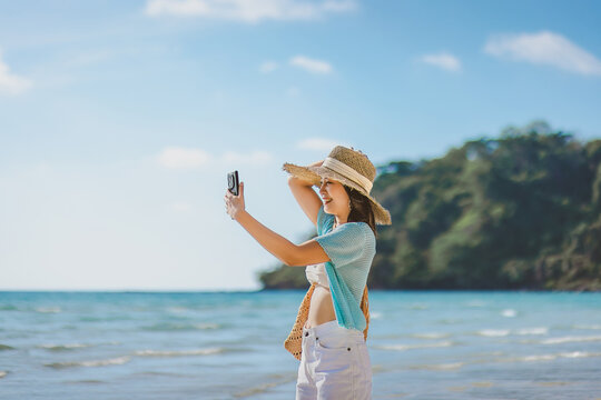 Happy asian traveler woman relax and use mobile phone for selfie on sea beach at day in Koh Kood Trat Thailand Travel summer holiday vacation concept