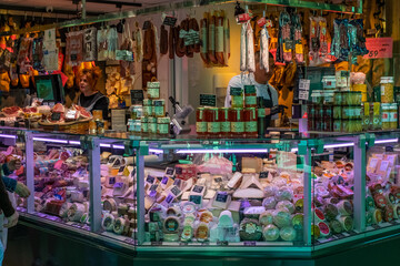 Meat and cheese delicatessen market stall displaying cured and smoked foods in a refrigerated cabinet for purchase. Selected preserves and gourmet provisions for sale.