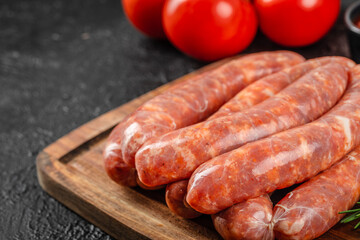 A close-up view of uncooked pork sausages stacked on a wooden cutting board with ripe red tomatoes in the background