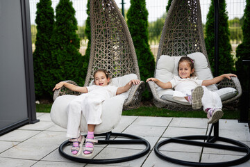 Two young girls enjoying relaxation on modern outdoor wicker egg-shaped chairs