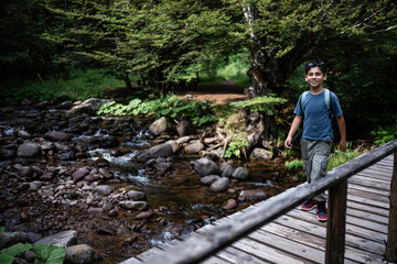 Young hiker crossing wooden bridge over mountain river in forest