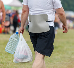 A man is walking with a bag on his back and a bottle in his hand