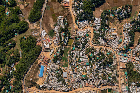 Aerial view of clustered buildings and winding pathways carve through the landscape, juxtaposing urban sprawl with natural greenery, Balukhali Bazar, Chittagong Division, Bangladesh.