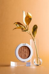 Bronzer makeup product shot with golden leaf and acrylic stands on peach background beauty