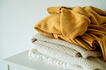 Warm cozy clothes on chest of drawers in home interior. Knitted autumn sweaters. Home organization.