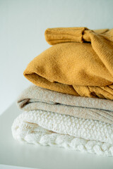 Warm cozy clothes on chest of drawers in home interior. Knitted autumn sweaters. Home organization.
