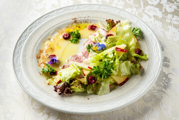 Gourmet dish of roasted meat slices topped with fresh salad, apple, cranberries, edible flowers,...
