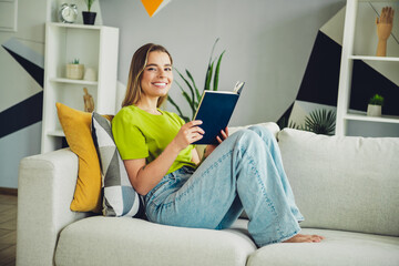 Young woman relaxing at home while reading a book, enjoying leisure time on a cozy sofa in a modern living room