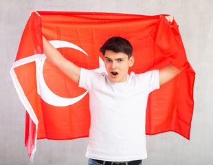 Young surprised guy teenager posing with big flag of Turkey in his hands in studio