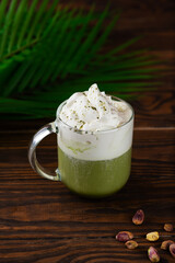 Pistachio green tea matcha latte in a glass with palm branch on table. Vertical orientation.