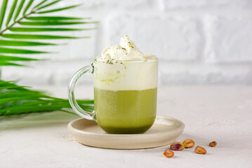 Pistachio green tea matcha latte with coconut milk in a glass with palm branch on table.