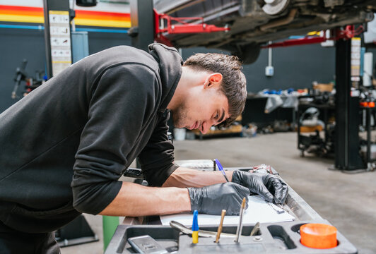 Young male mechanic filling out technical form during vehicle maintenance