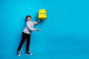 Cheerful boy presenting a bright yellow backpack against a vibrant blue background showcasing school spirit and energy