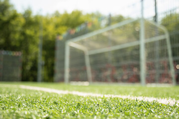 Blurred empty soccer goal on field with focus on artificial green grass. Summer outdoor game....