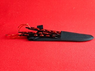 A set of several throwing knives in a case for combat training and sport throwing on a red background.