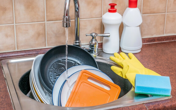 Close up of dirty dishes in kitchen sink with running water and cleaning supplies washing dishes faucet - Powered by Adobe