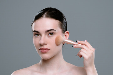 Fototapeta premium Young Woman Applying Makeup Using a Brush on Her Face