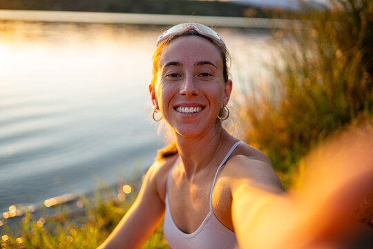 Sportswoman taking selfie by the lake at sunset after training