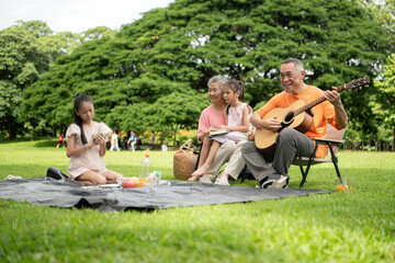 Happy Asian grandparents enjoying a picnic with their granddaughter in a green park